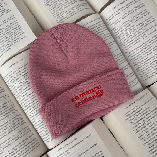 Pink beanie with 'romance reader' embroidery on an open book