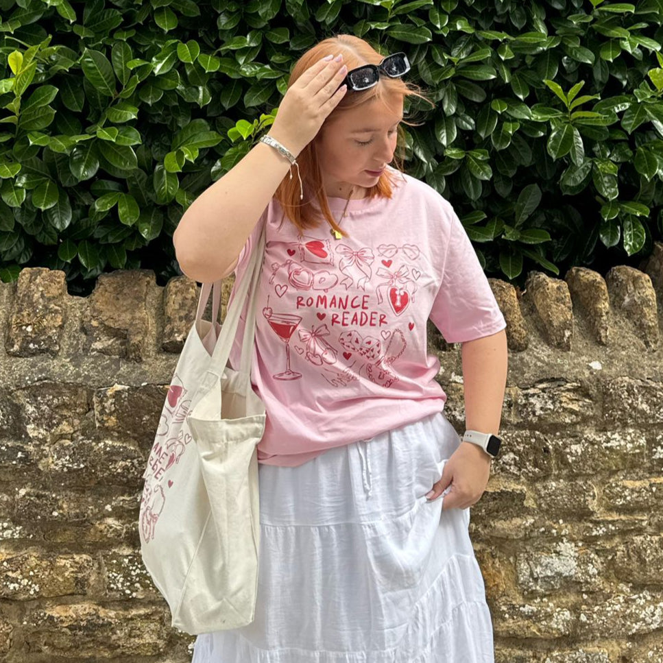 Woman in a pink shirt and white skirt standing in front of a stone wall and green bush