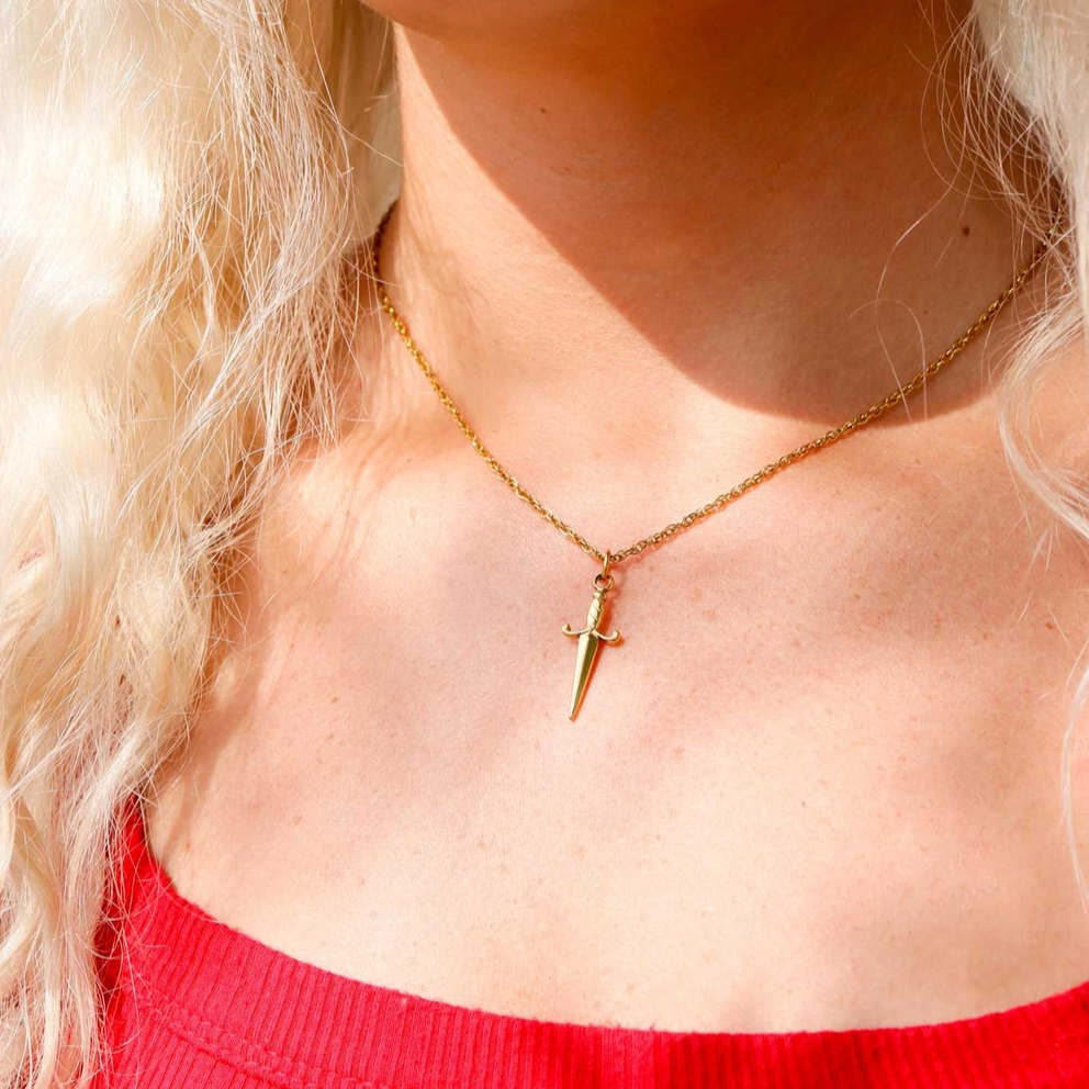 Close-up of a person wearing a gold necklace with a small pendant, against a blurred background.