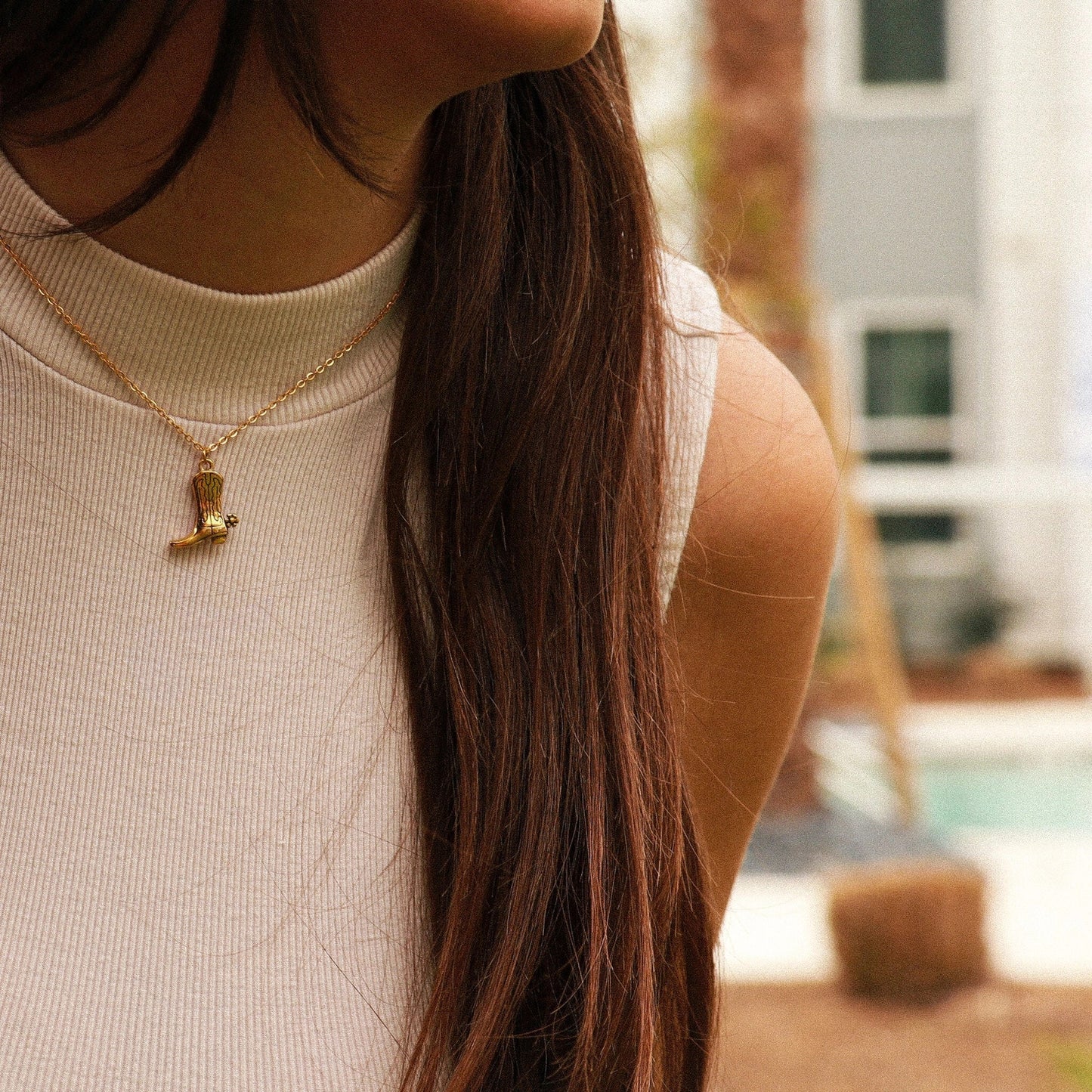 Close-up of a person wearing a gold necklace with a pendant, blurred background