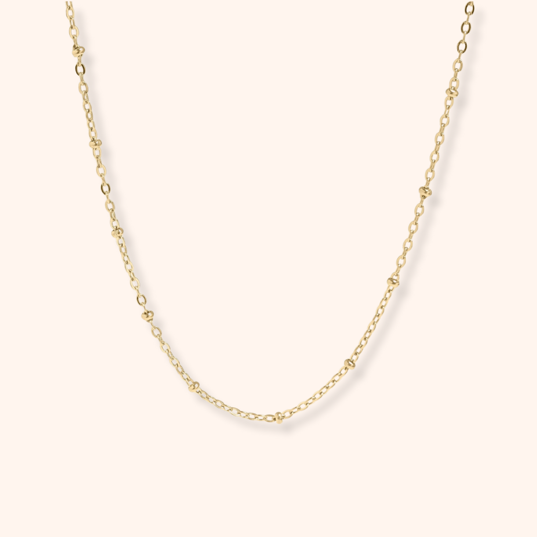 Gold chain necklace on a light pink background