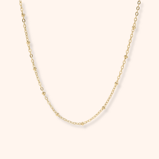Gold chain necklace on a light pink background