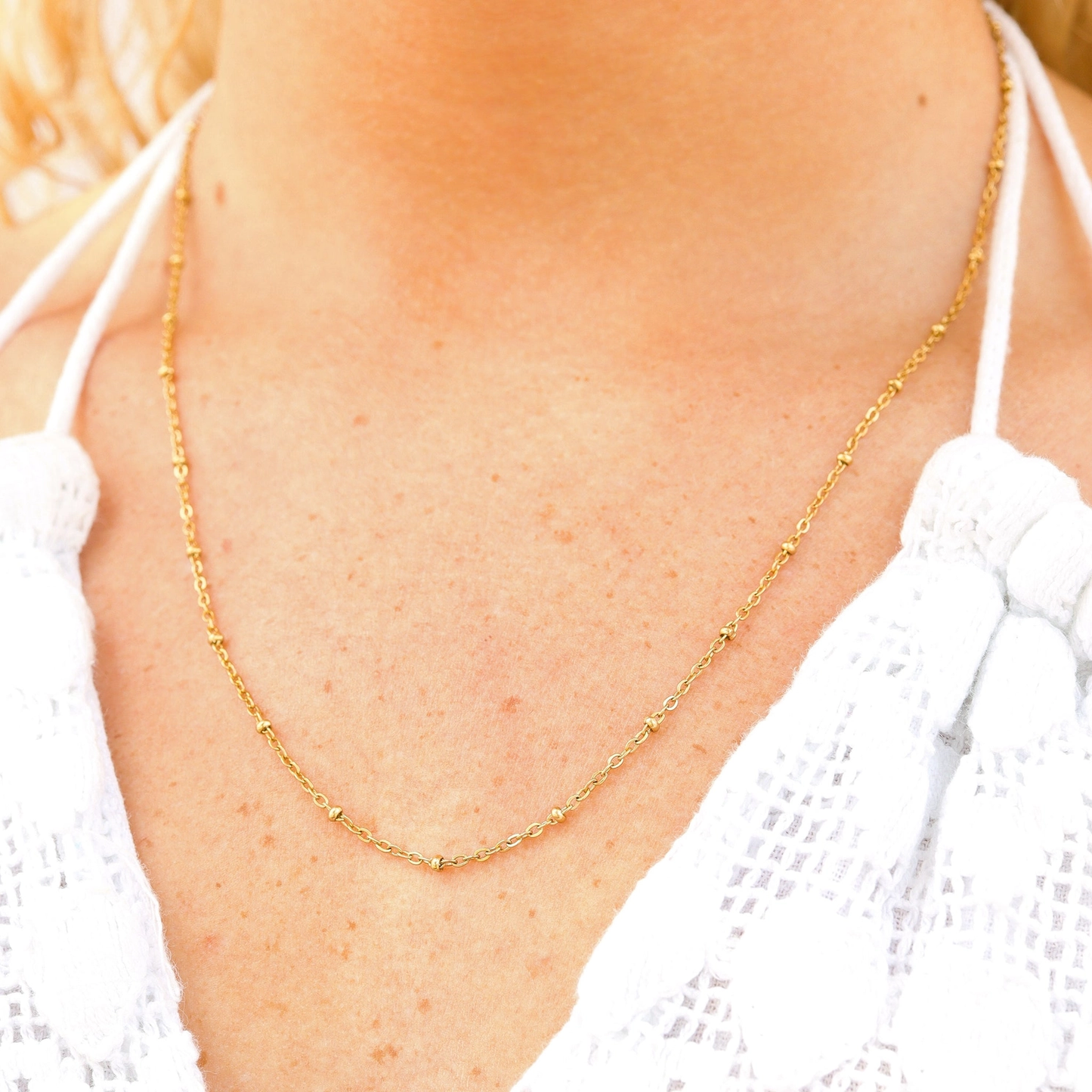 Gold necklace on a person wearing a white top
