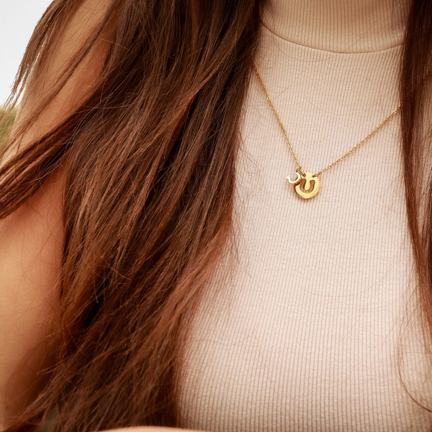 Gold necklace with a pendant worn by a person with long brown hair.