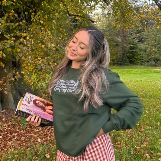 Woman holding a book outdoors in a park with trees and grass.