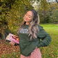 Woman holding a book outdoors in a park with trees and grass.