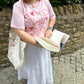 Person wearing a pink 'Romance Reader' t-shirt holding an open book against a stone wall.