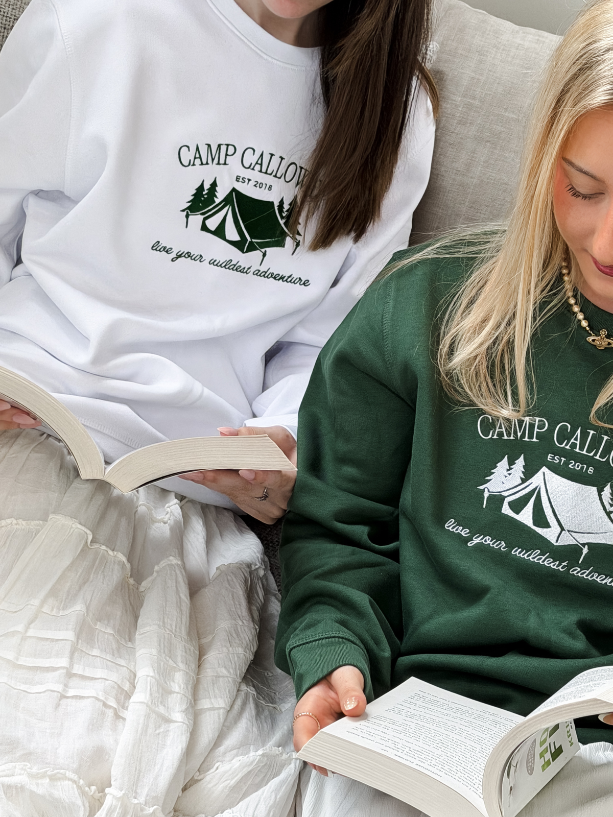 Two people wearing 'Camp Calloway' sweatshirts, one white and one green, sitting on a couch reading books.
