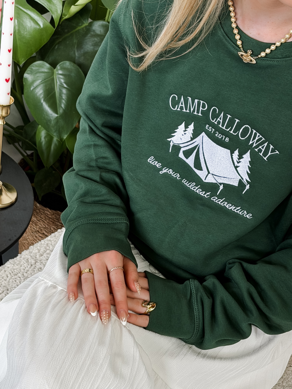 Person wearing a green sweatshirt with 'Camp Calloway' design, sitting indoors.