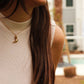 Close-up of a person wearing a gold necklace with a pendant, blurred background