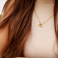 Gold necklace with a pendant worn by a person with long brown hair.