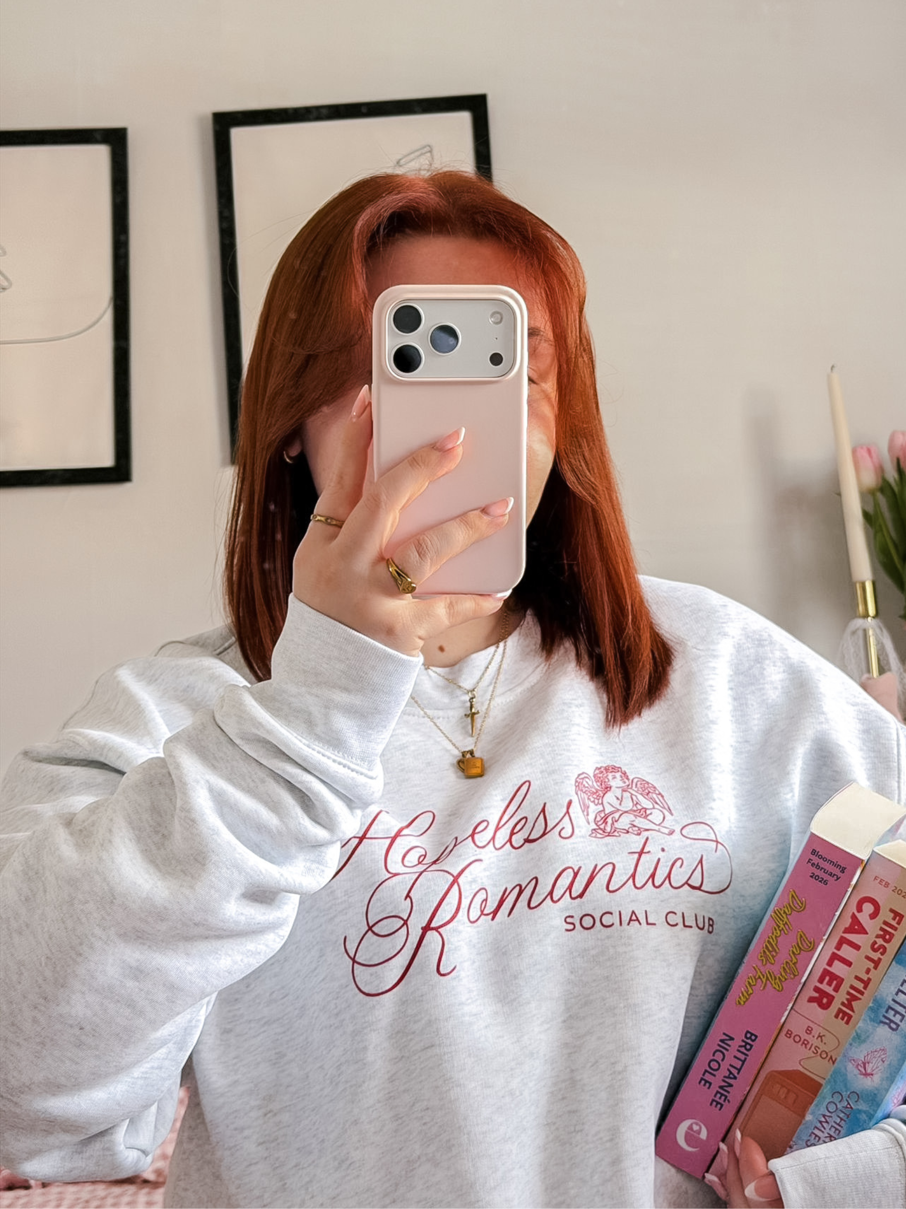 Person wearing a light grey sweatshirt with 'Hopeless Romantics Social Club' text, holding a phone.