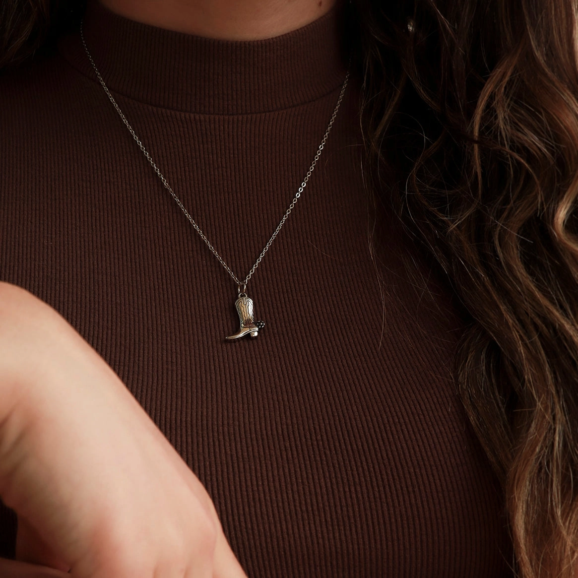 Person wearing a necklace with a cowboy boot pendant on a brown background